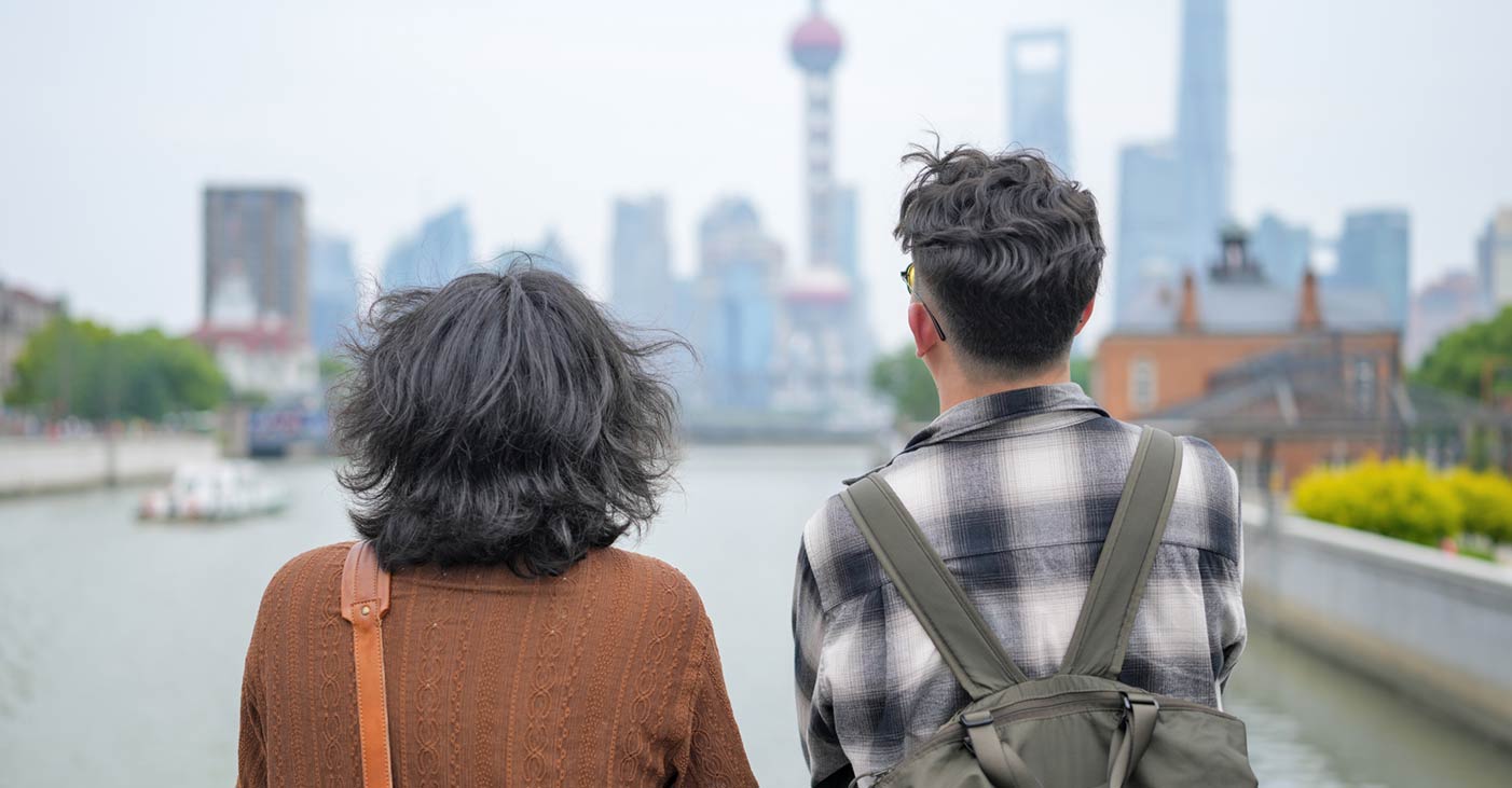 Two young Chinese men looking across water at a city in the distance